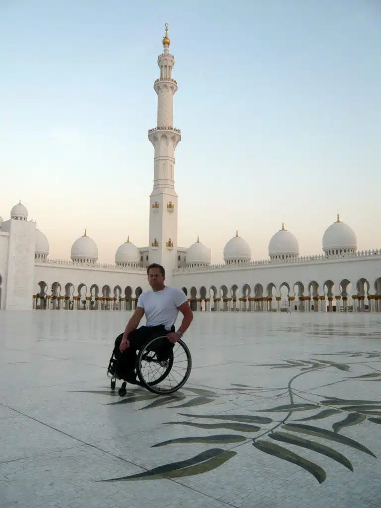 Staffan är på arbetsresa som Rehabinstruktör i Abu Dhabi 2009. Han står på ett vitt mönstrat marmorgolv och orientaliska torn i bakgrunden i Schejk Zayed-moskén. Han har på sig vit T-shirt och svarta byxor.