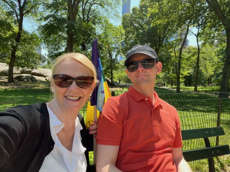 Jeanette och André Fridh sitter i Central Park i New York då de besökte en funktionsrättsorganisation i staden. Jeanette har långt blont hår, solglasögon, klädd i en svart tröja och vit topp. André sitter bredvid klädd i en mörk keps, solglasögon, röd pikétröja. Bakom syns gröna buskar och träd.