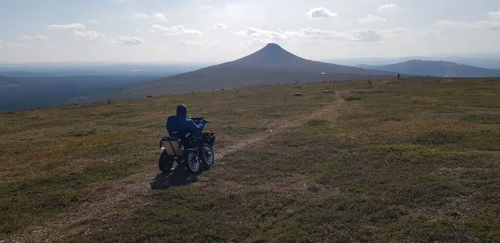 Anders åker i öppen terräng uppför en backe i fjälltrakten sittandes på en eldriven terränganpassad rullstol.