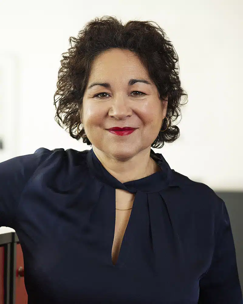 Profilbild Sabina Rasiwala. Hon har mörkbrunt axellångt lockigt hår, ljus hy och ett mörkblått klädesplagg på överkroppen.